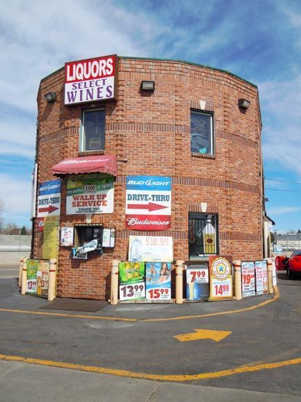 Brick liquor store on a corner, with colorful sale signs and a red awning.