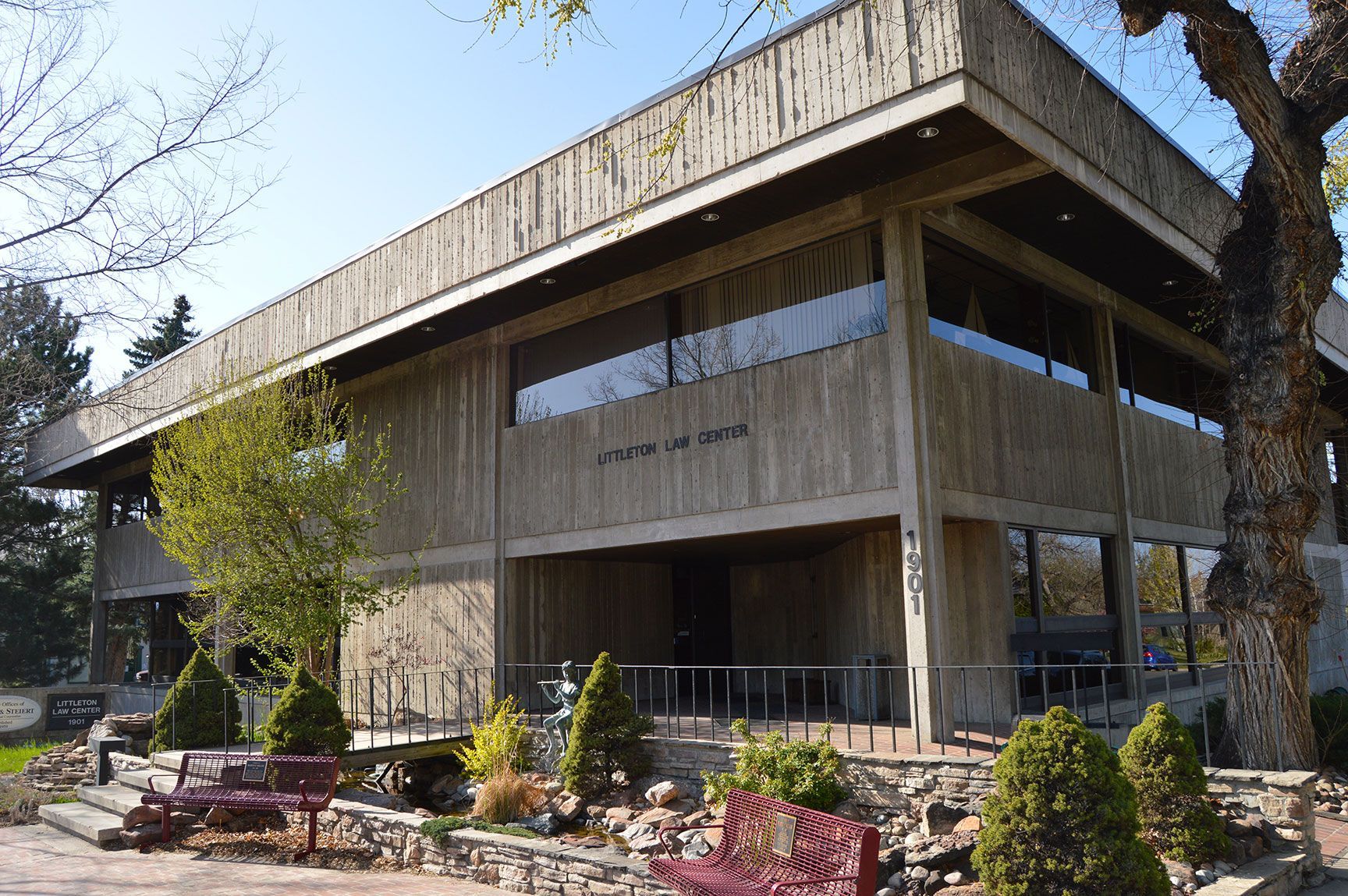 Modern two-story building with large windows, wooden siding, and landscaped plants in front