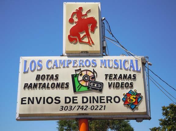 Sign for Los Camperos Musical with boots, pants, jeans, videos, and money transfer services under a red dancer