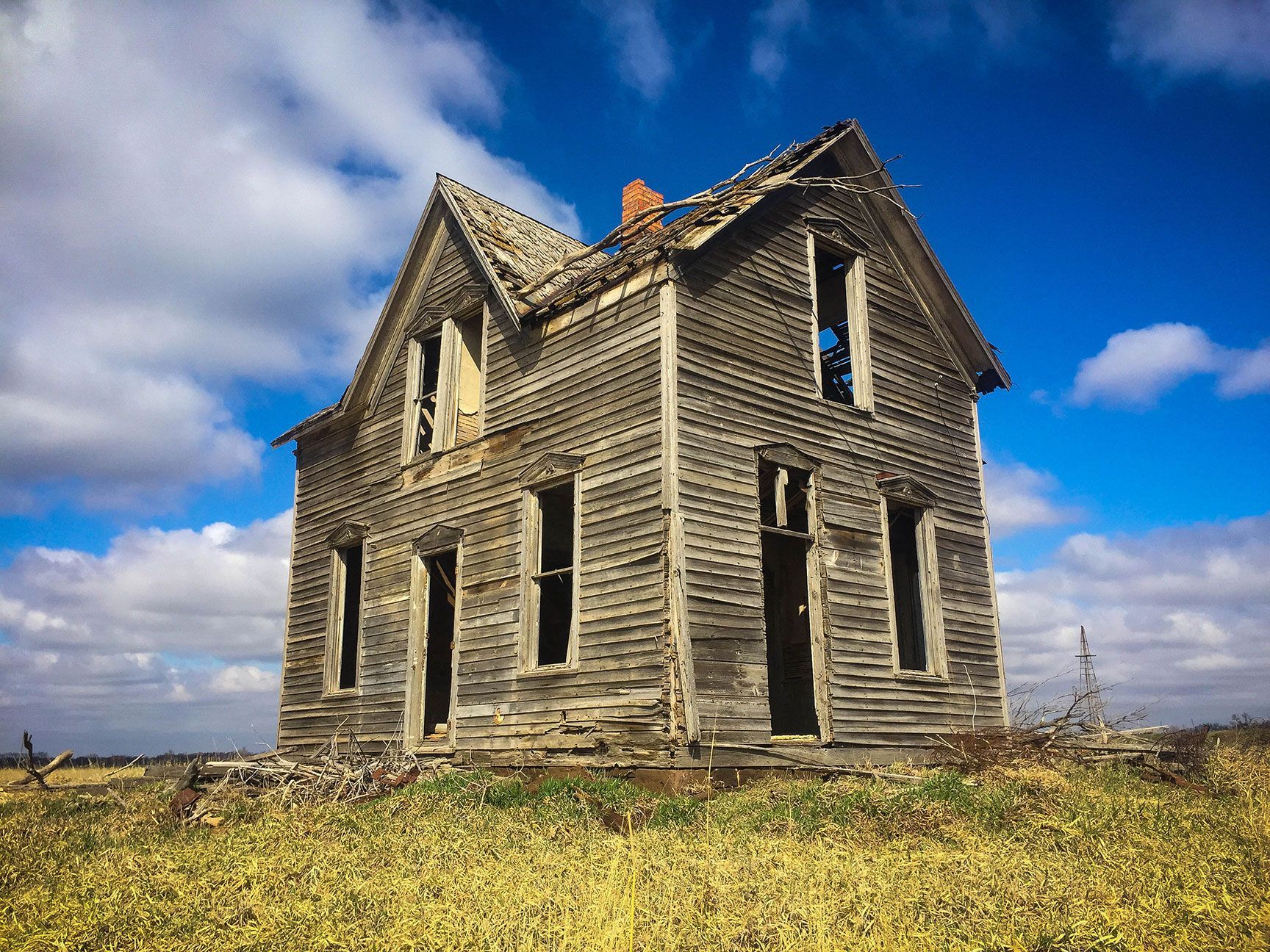 Abandoned wooden house on a grassy field under a blue sky with clouds