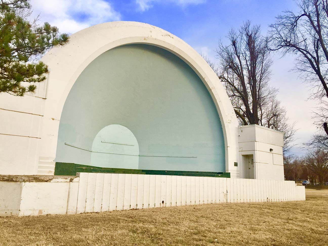 Outdoor white shell amphitheater with a pale green stage and trees in the background