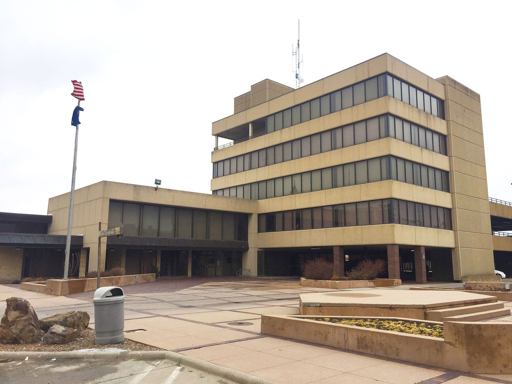 Modern tan office building with a U.S. flag in front and a paved plaza under construction