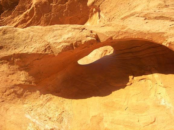 Sunlit sandstone arch in a desert canyon with a dark shadowed opening