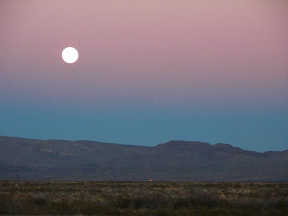 Full moon over a mountain ridge at dusk with a pink and blue sky