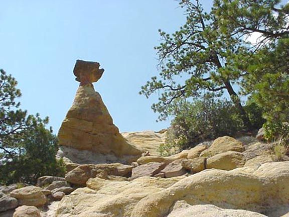 Stacked rocks on a sunlit rocky outcrop under a clear blue sky, with trees in the background