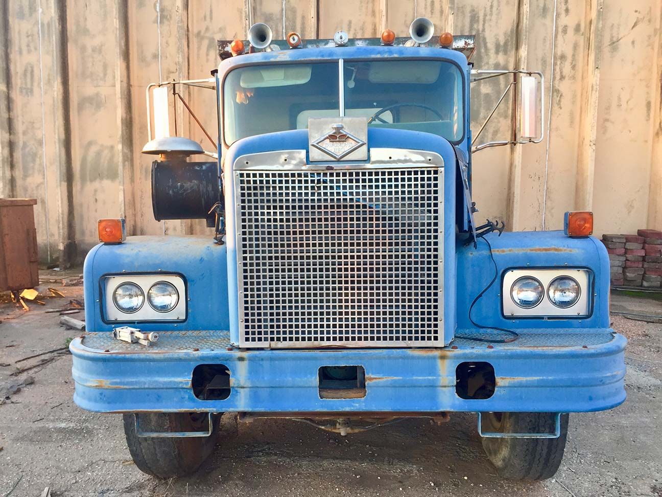 Front view of a blue semi truck with a chrome grille parked against a wooden wall, Salina, Kansas