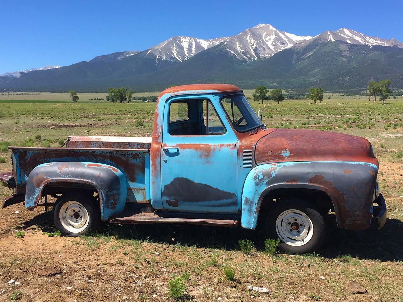 Rusty blue pickup truck in a field with mountains in the background, Buena Vista, Colorado