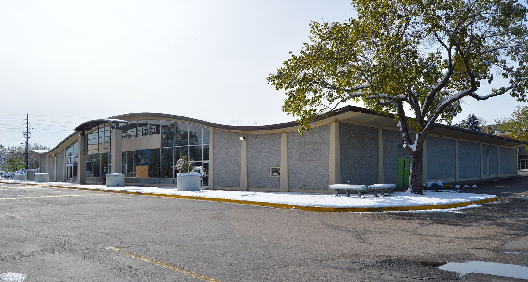 Single-story brick building with glass entrance and a tree in front on a snowy street.
