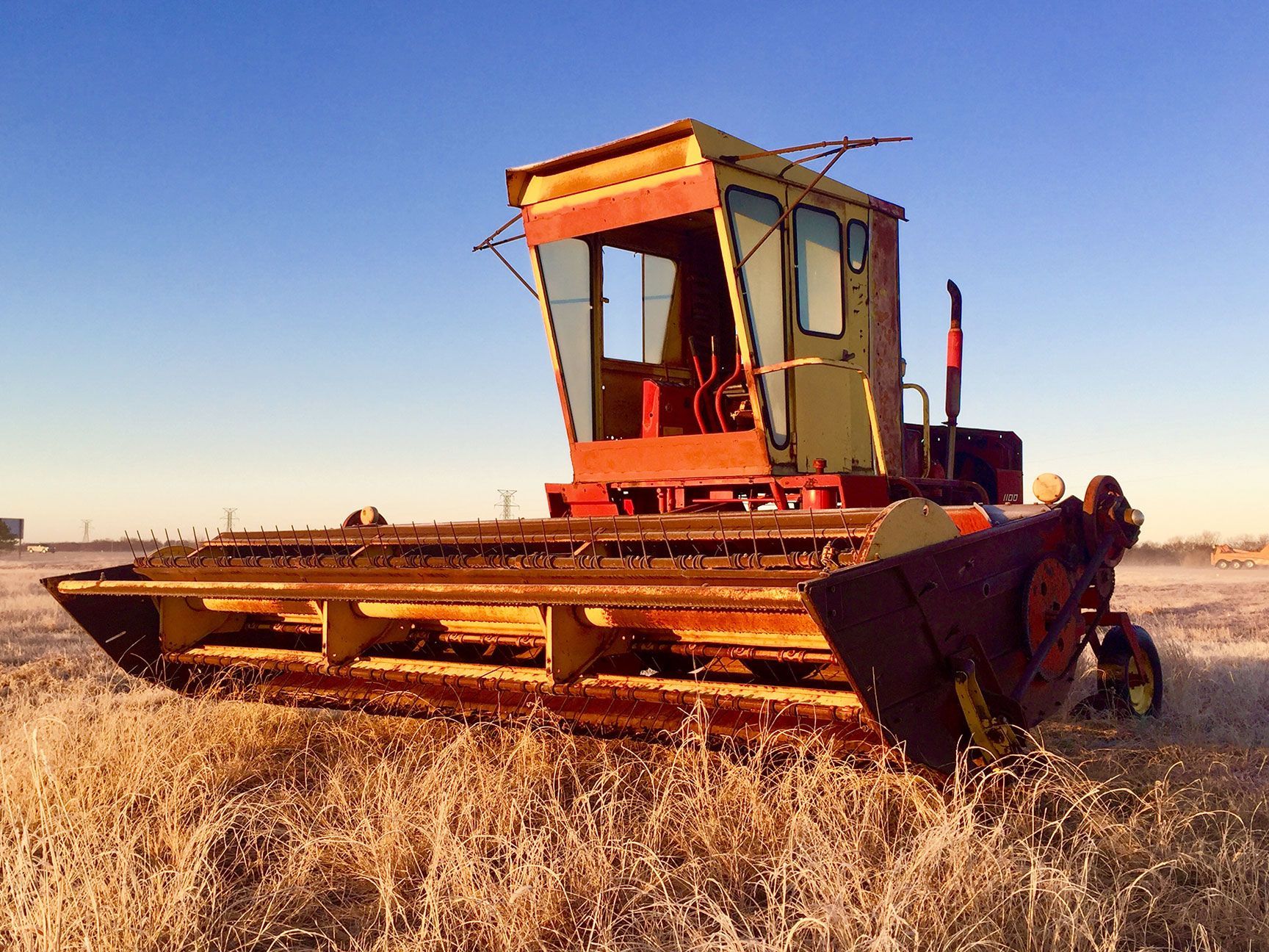 Orange combine harvester in a dry field at sunset