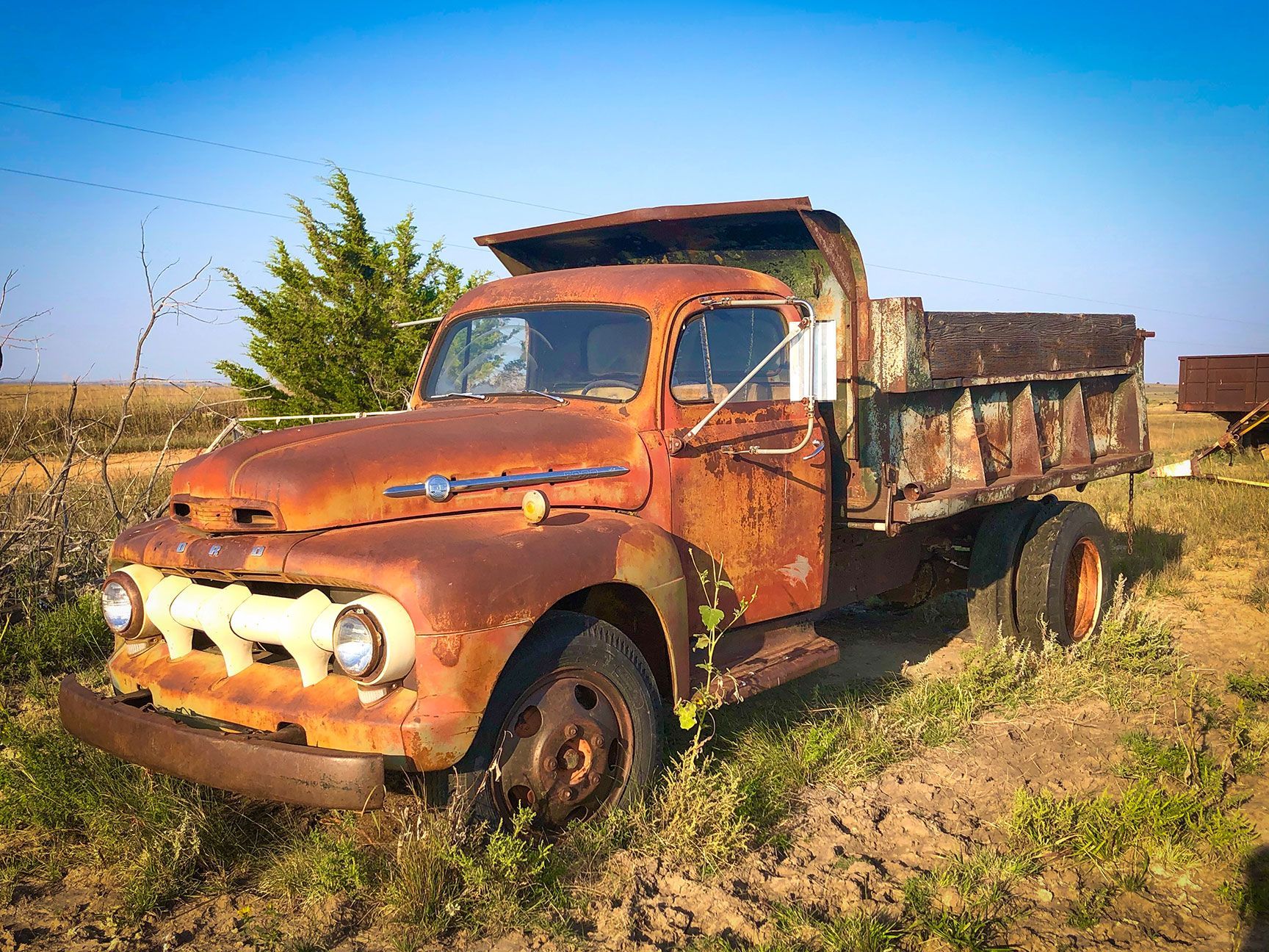 Rusty old pickup truck abandoned in a grassy field under a clear blue sky