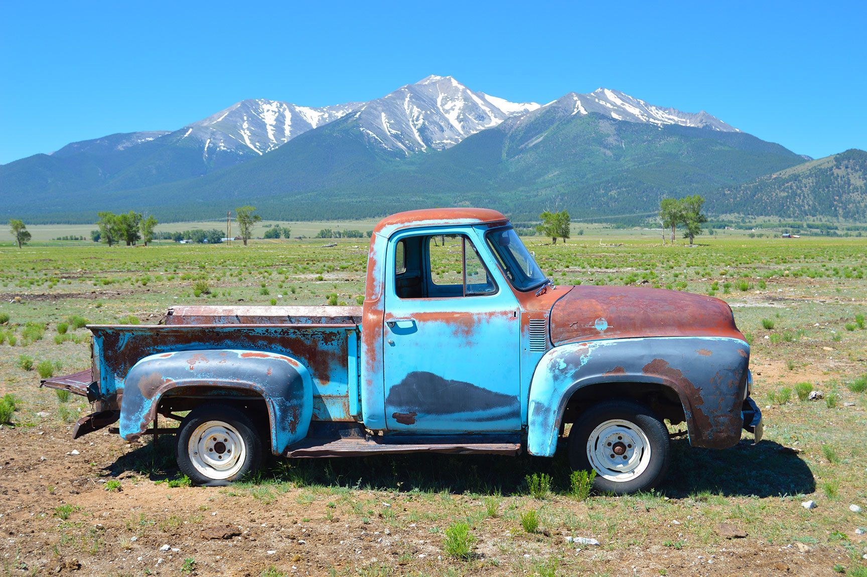 Rusty blue pickup truck in a field with snow-capped mountains in the background, Buena Vista, Colorado
