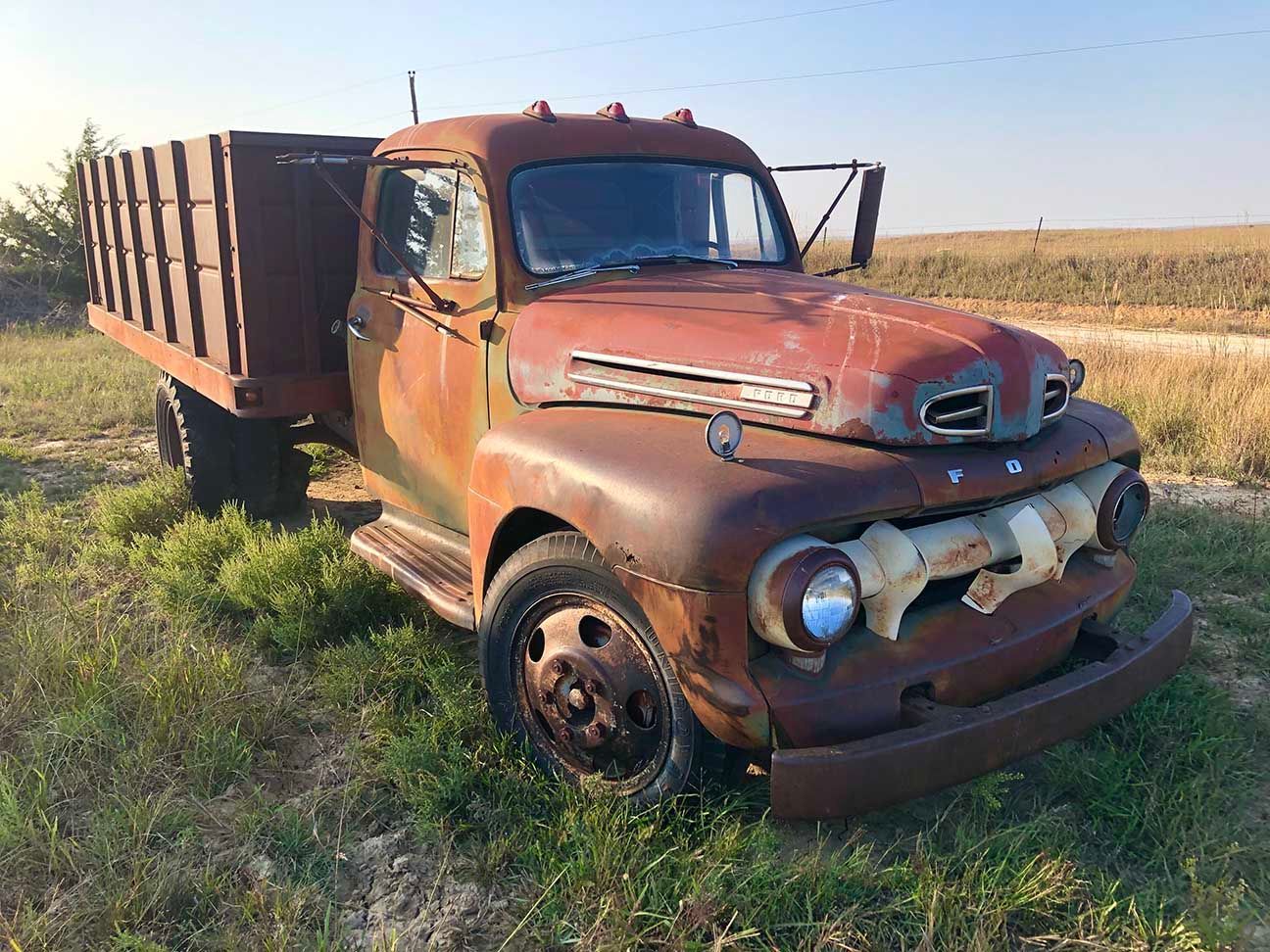 Rusty vintage dump truck parked in a grassy field under clear sky, Salina, Kansas