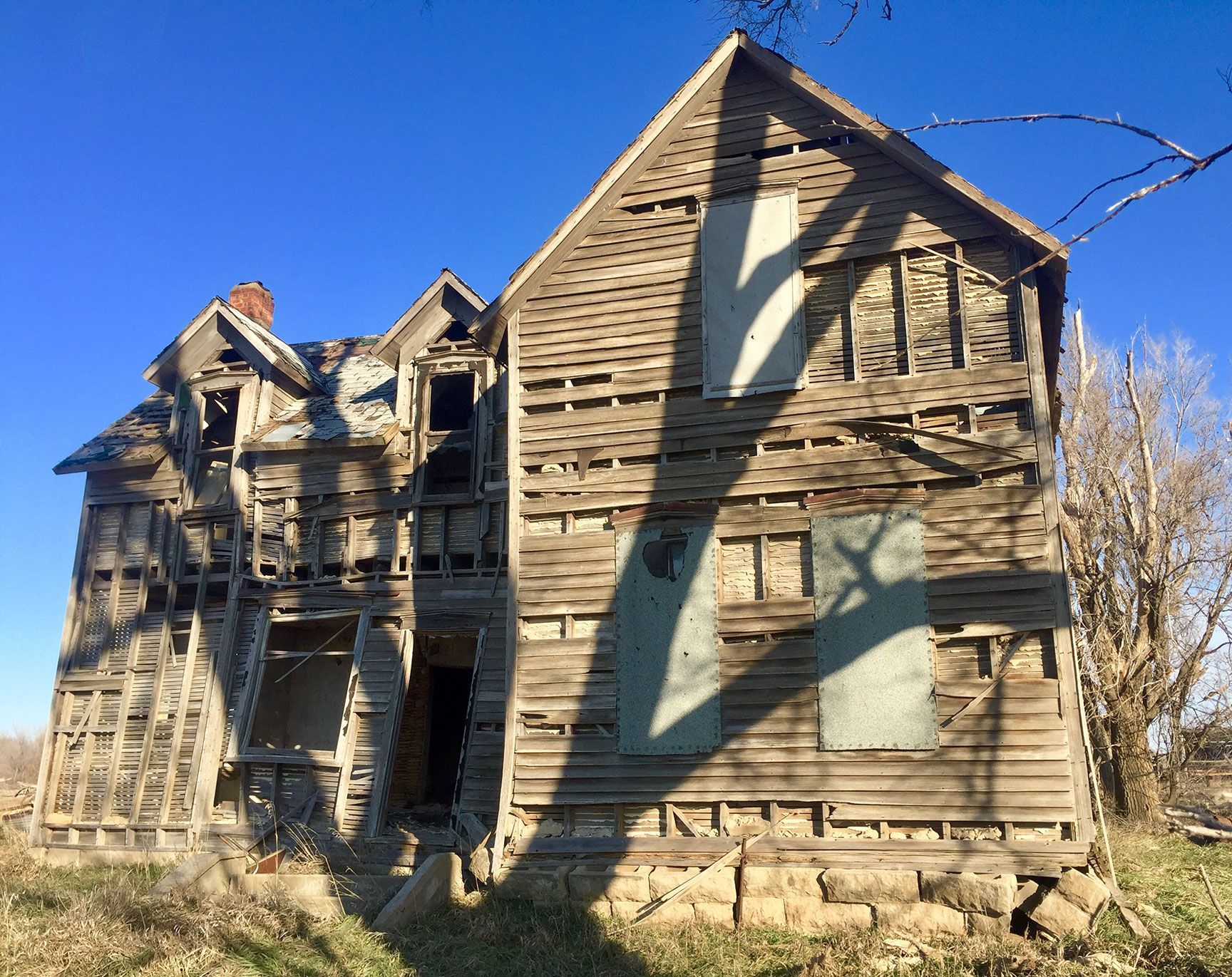 Old weathered wooden house with severe structural damage, seen in sunlight under a blue sky.