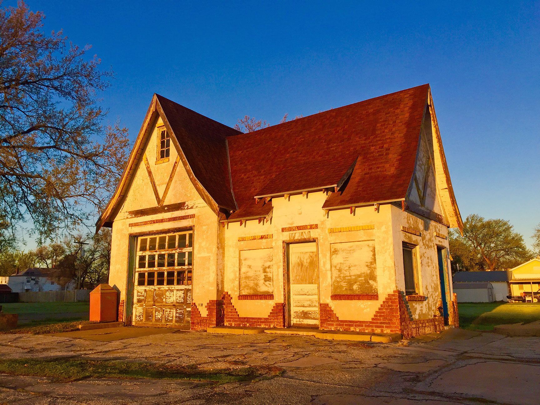 Small cream house with red roof in warm sunlight on a dirt lot against a blue sky