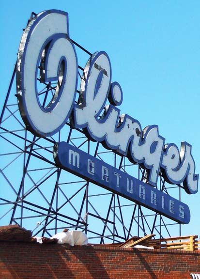 Old Olympia sign against blue sky with blue “mattress” banner and rooftop foreground
