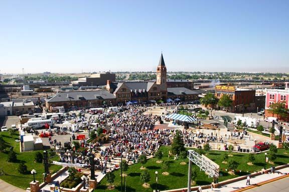 Large crowd gathered in a town square near a church and park under a clear blue sky