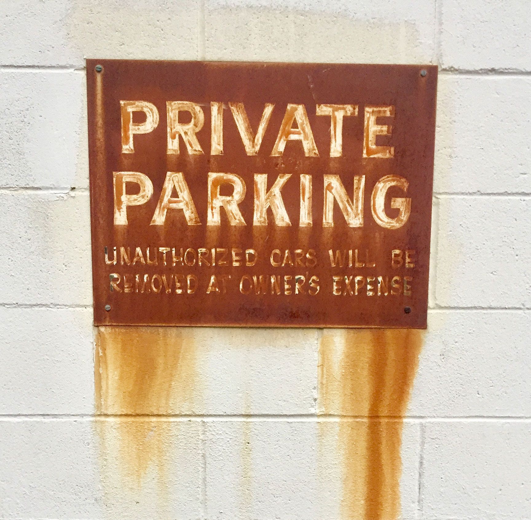 Rusty red PRIVATE PARKING sign on a white wall with rust stains below.