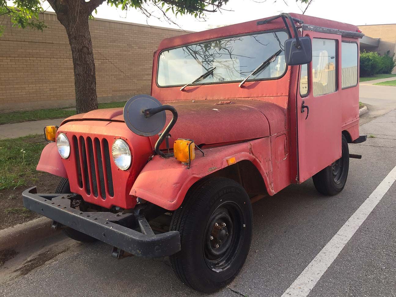 Red vintage jeep parked by a roadside with trees and a stone wall, Salina, Kansas