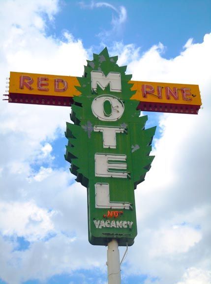 Red Pine Motel roadside sign shaped like a green pine tree against a cloudy blue sky