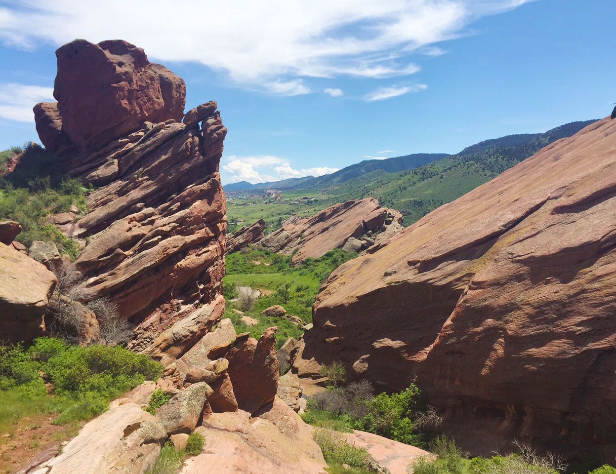 Red sandstone rock formations in a green valley under a blue sky with clouds, Red Rocks, Morrison, Colorado