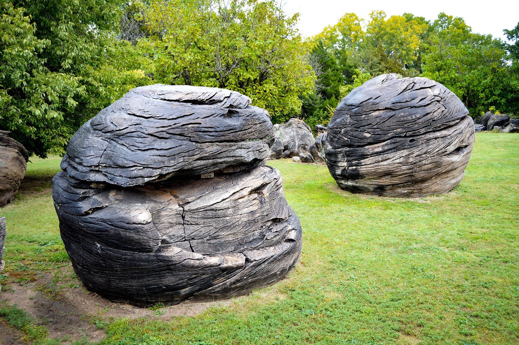 Two large dark stone sculptures in a grassy park with trees in the background