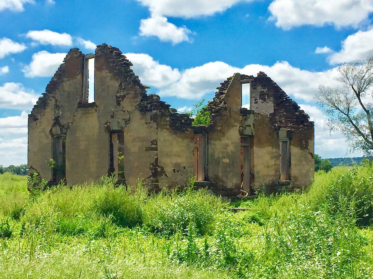 Ruins of a stone building in a grassy field under a bright blue sky with clouds