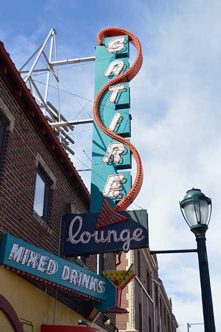 Vertical neon sign for an Italian lounge restaurant on a city street, with blue sky above