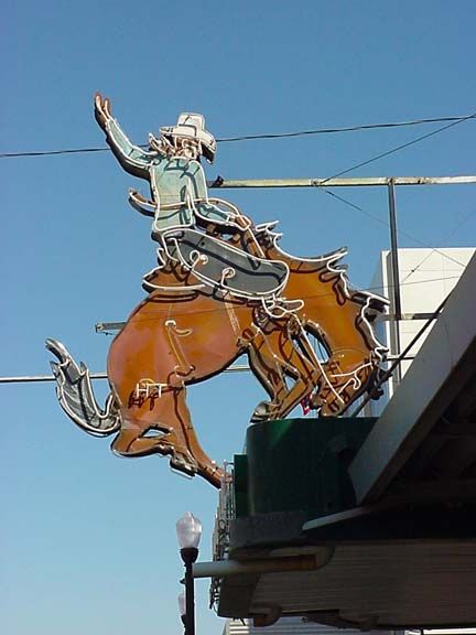 Cowboy on a bucking bronco neon sign against a blue sky