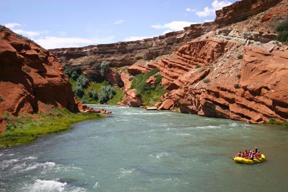 Rafting boat on a green river between red canyon cliffs under a blue sky