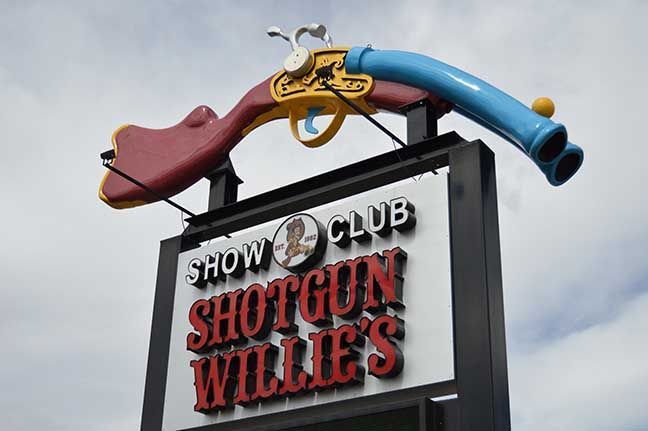 Neon cowboy sign for Show Club Shotgun Willie's with a blue shotgun and red boot on top