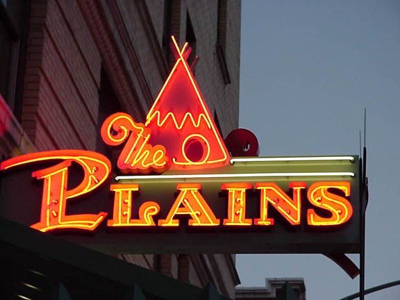 Neon sign reading “The Plains” above a building at dusk