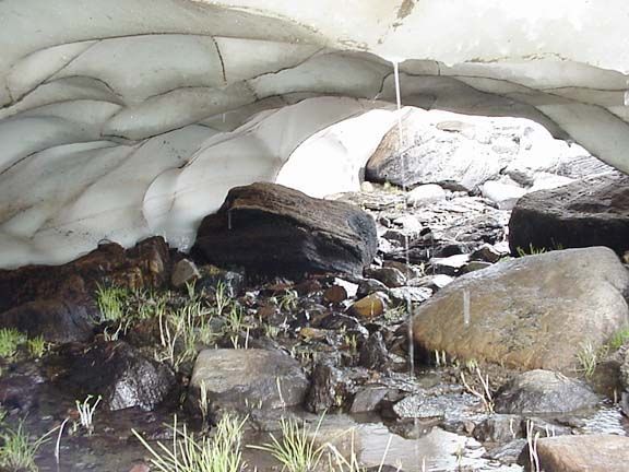 Snow cave over a rocky stream with boulders and moss inside, Snowy Range, Wyoming