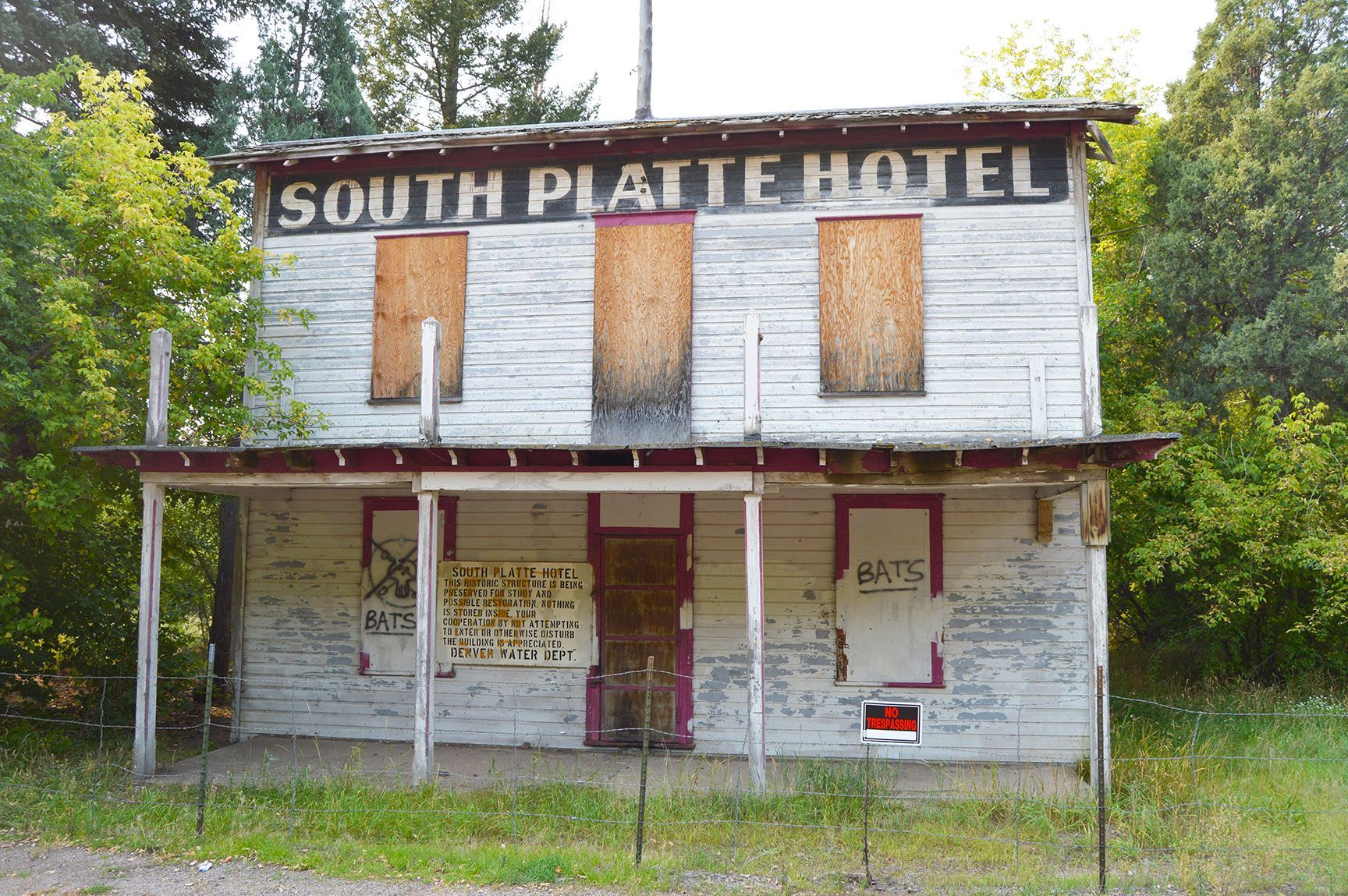 Abandoned South Platte Hotel, boarded windows, weathered white facade, overgrown foreground, Colorado