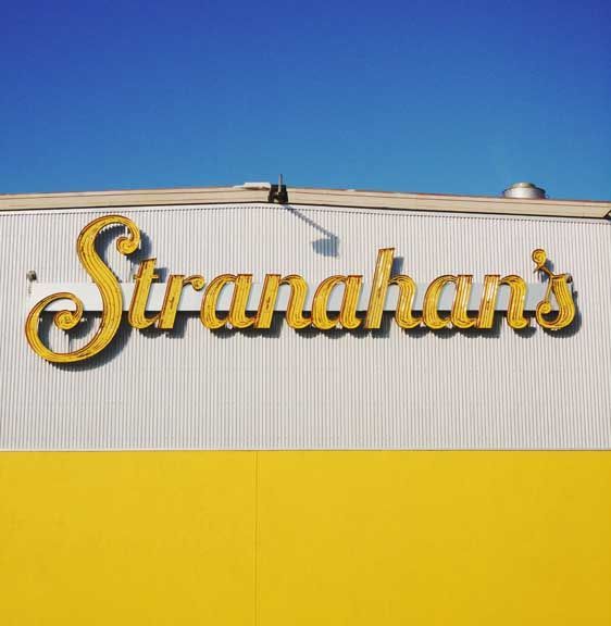 Stranahan’s sign on a corrugated building with yellow lower facade and blue sky above