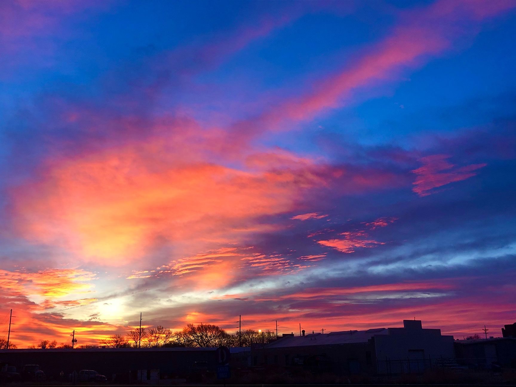Vibrant sunset sky with pink, orange, and blue clouds over silhouetted buildings and trees