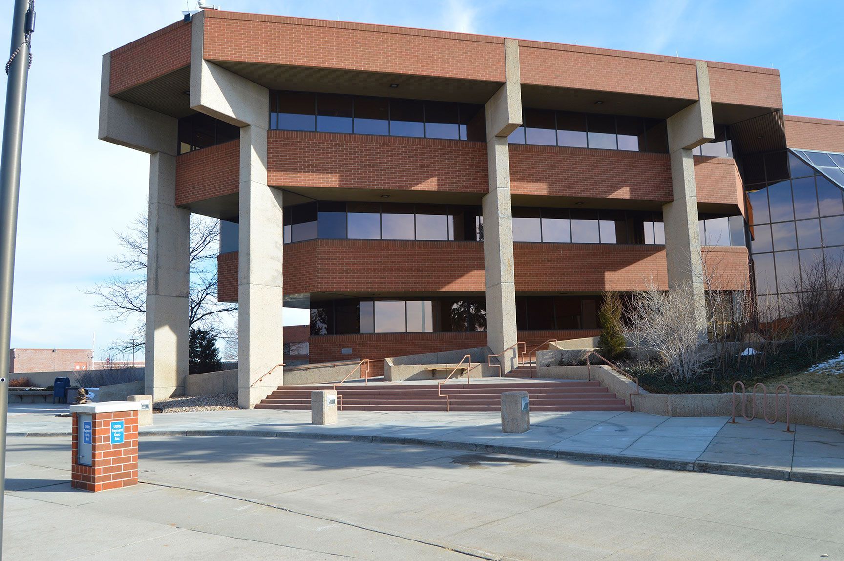 Modern concrete building with red-tiled roof and open columns beside a street