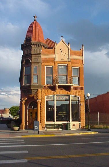 Historic brick corner building with red turret and large storefront windows on a city street