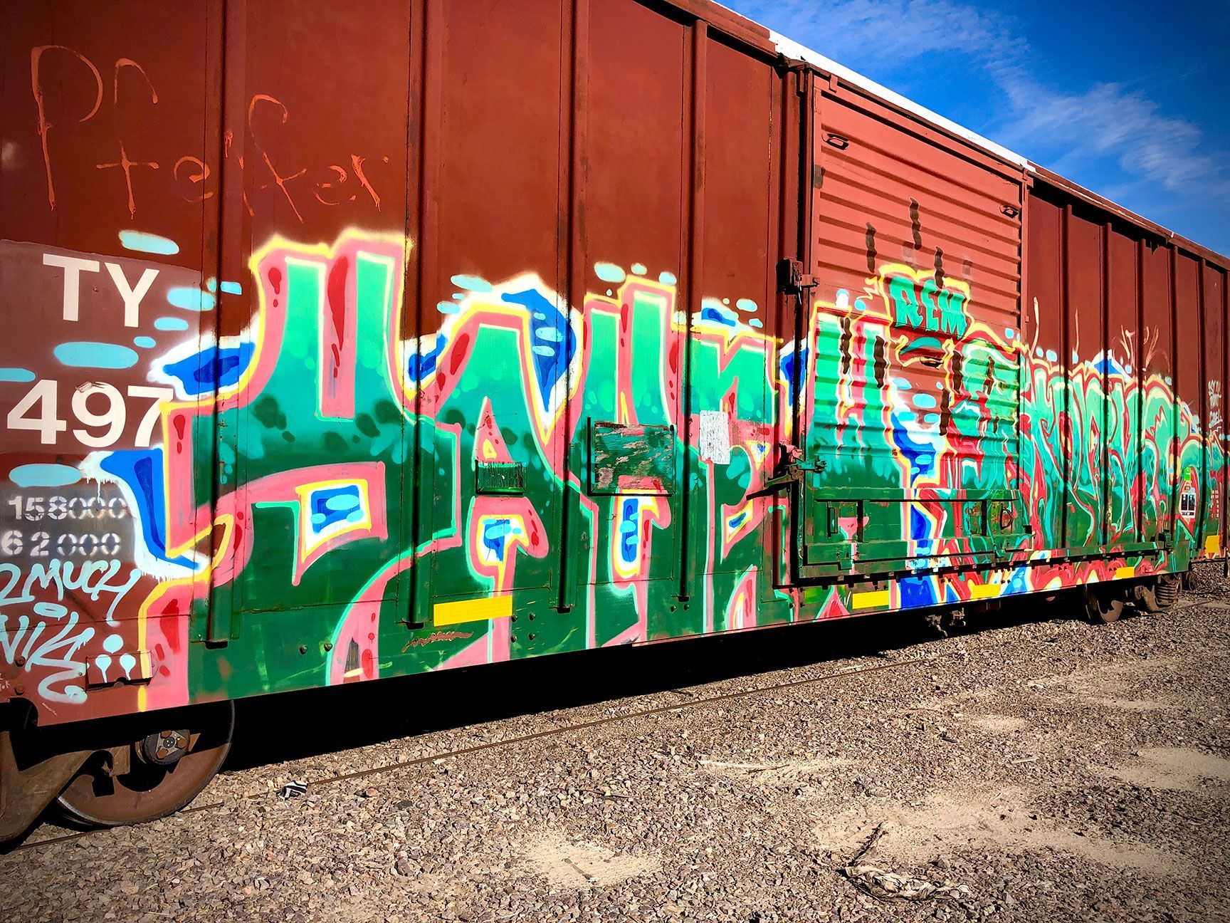 Graffiti-covered rusty freight boxcar on railroad tracks under a blue sky