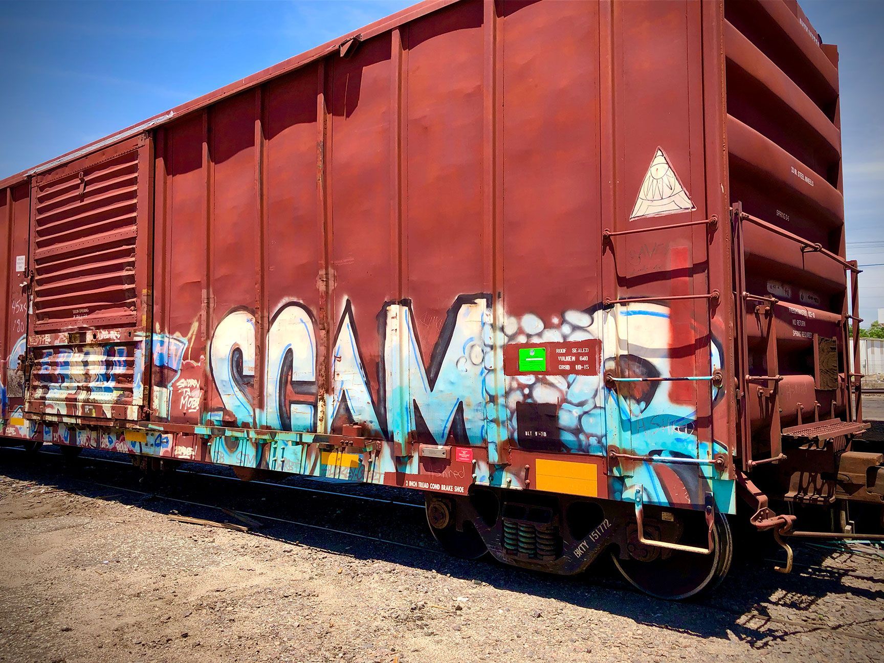 Red freight train car with colorful graffiti on tracks in a sunny outdoor yard.