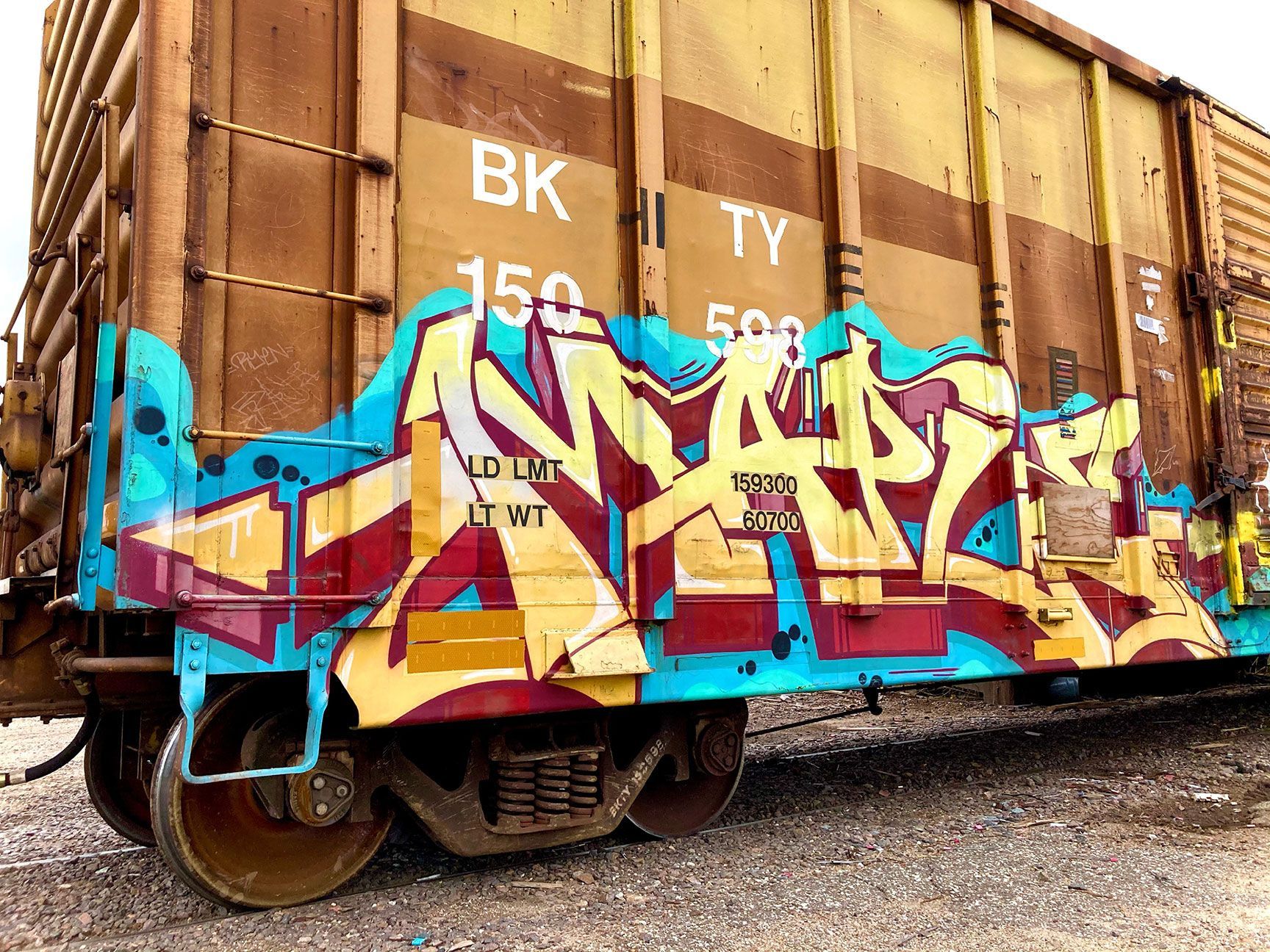 Graffiti-covered rusty freight boxcar in brown and tan on gravel tracks