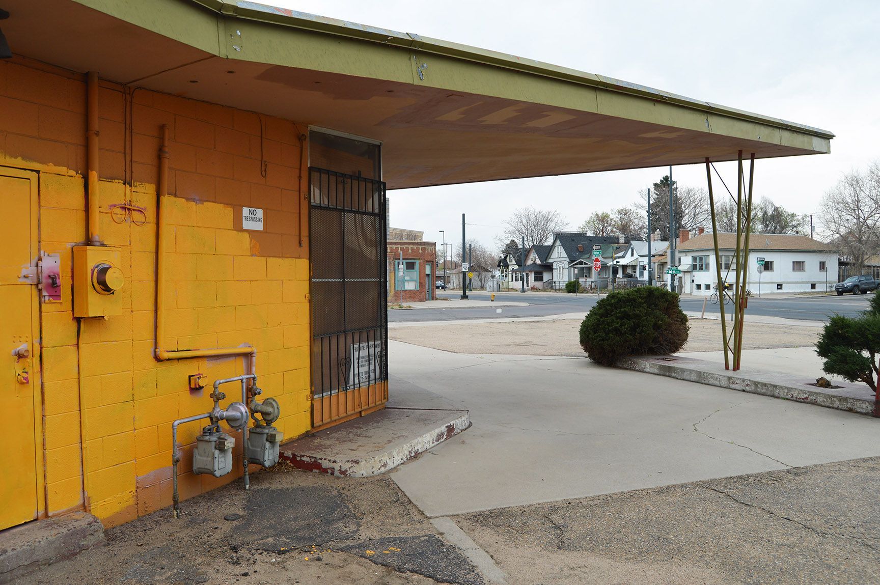 Orange building corner with a small covered entrance, parking lot, and a trimmed bush outside