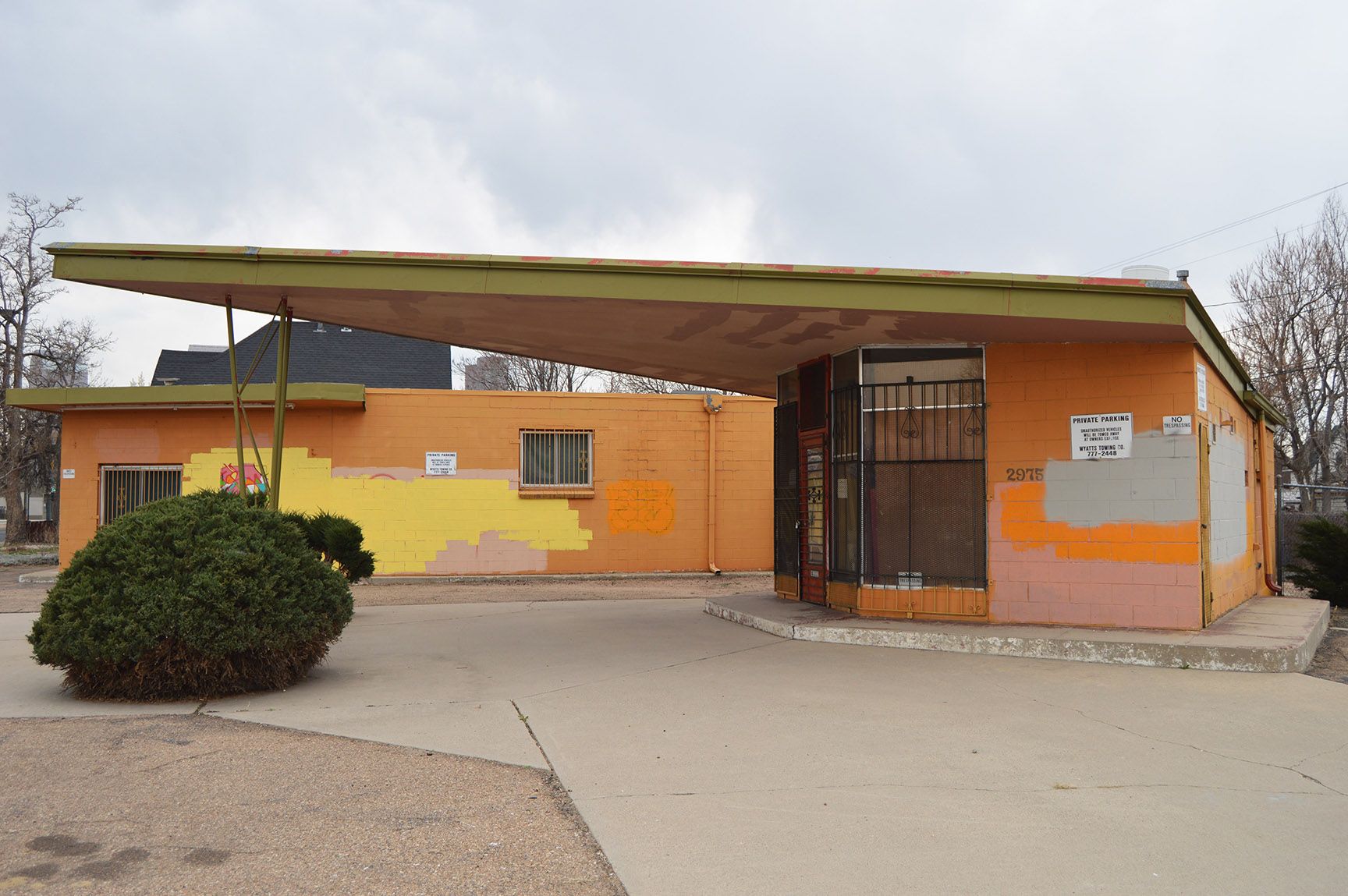 Orange building with a wide overhang, gated entrance, and a small bush in front