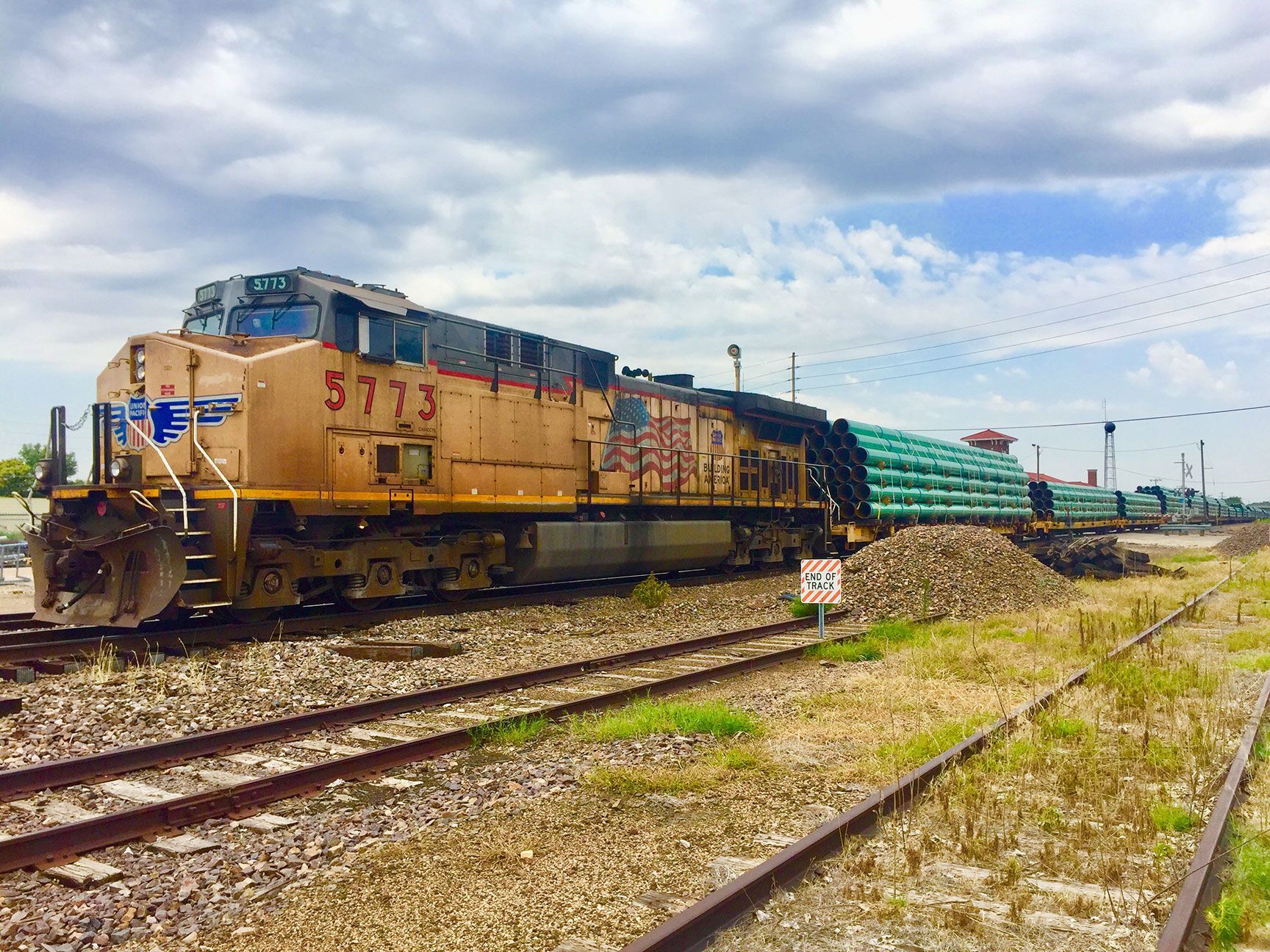 Freight train with yellow locomotives and green cars on tracks under a cloudy sky
