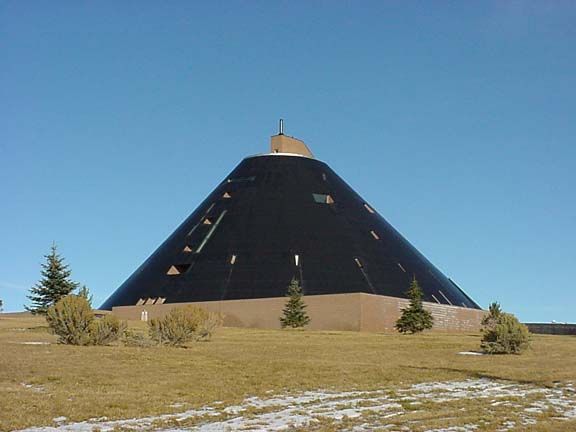 Large conical black building with small windows on a grassy hill under a clear blue sky