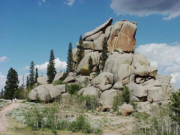 Large granite boulder formation with pine trees and a dirt path under a blue sky, Vedauwoo State Recreation Area, Wyoming
