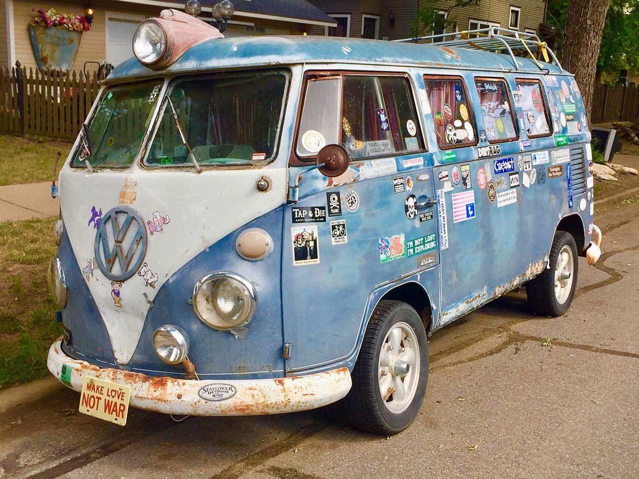 Vintage blue-and-white Volkswagen van covered in stickers, parked outdoors on a street, VW-bus, Salina, Kansas