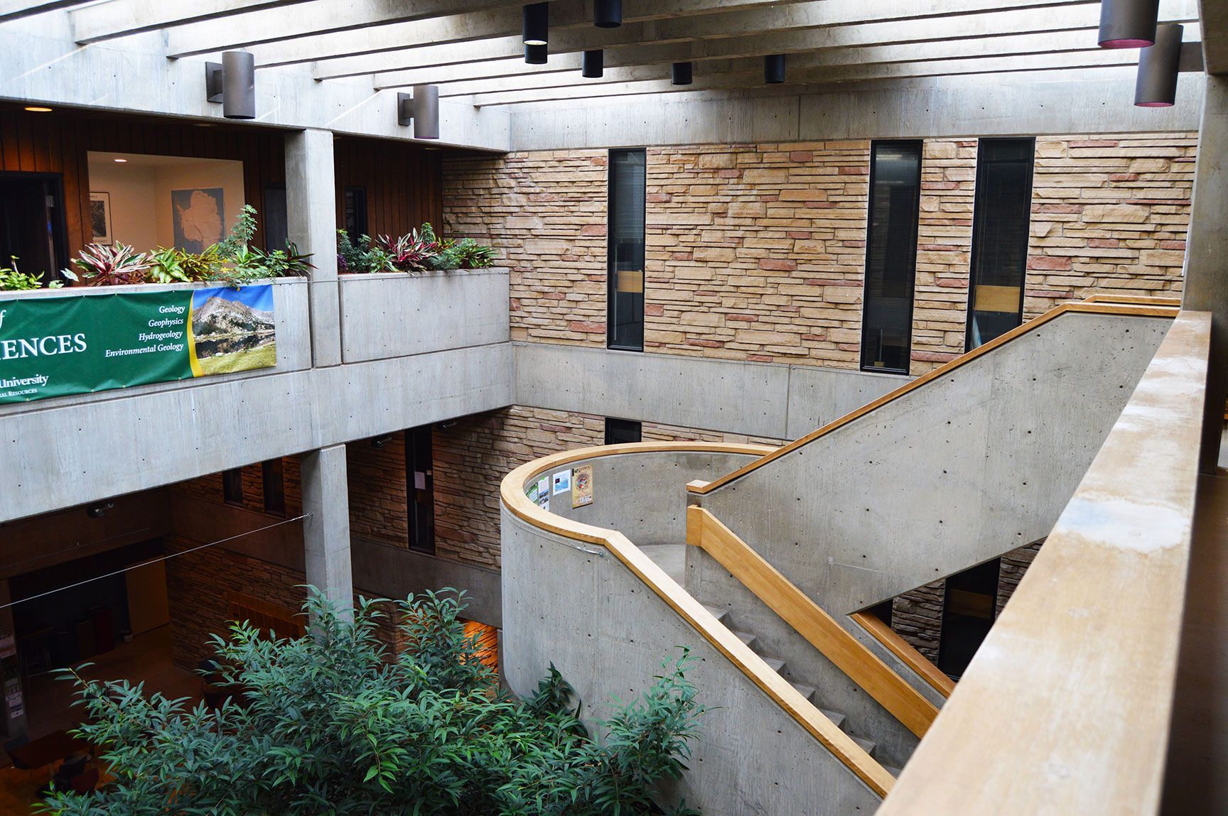 Indoor atrium with curved ramp, stone walls, balconies, and greenery in a modern building