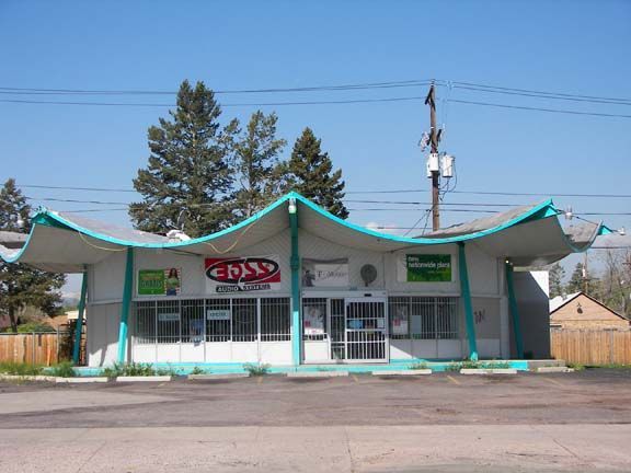 Small storefront with teal trim and awnings under a clear blue sky, seen from the street.