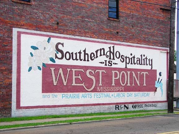 Mural on brick wall reading “West Point, Mississippi,” with “Southern Hospitality” and “Prairie Arts Festival.”