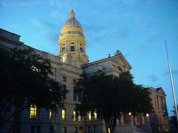 Illuminated historic domed building at dusk with trees in front under a blue sky